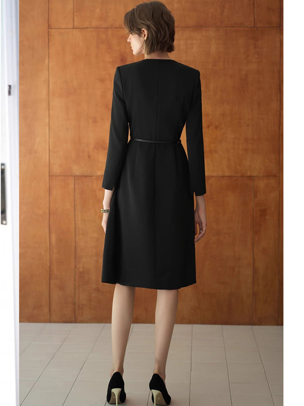 A stylish, elegant dress in trench coat style with a fitted waistline, a round neckline, and a long, flowing skirt in black.