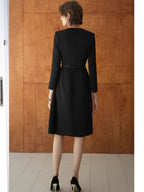 A stylish, elegant dress in trench coat style with a fitted waistline, a round neckline, and a long, flowing skirt in black.