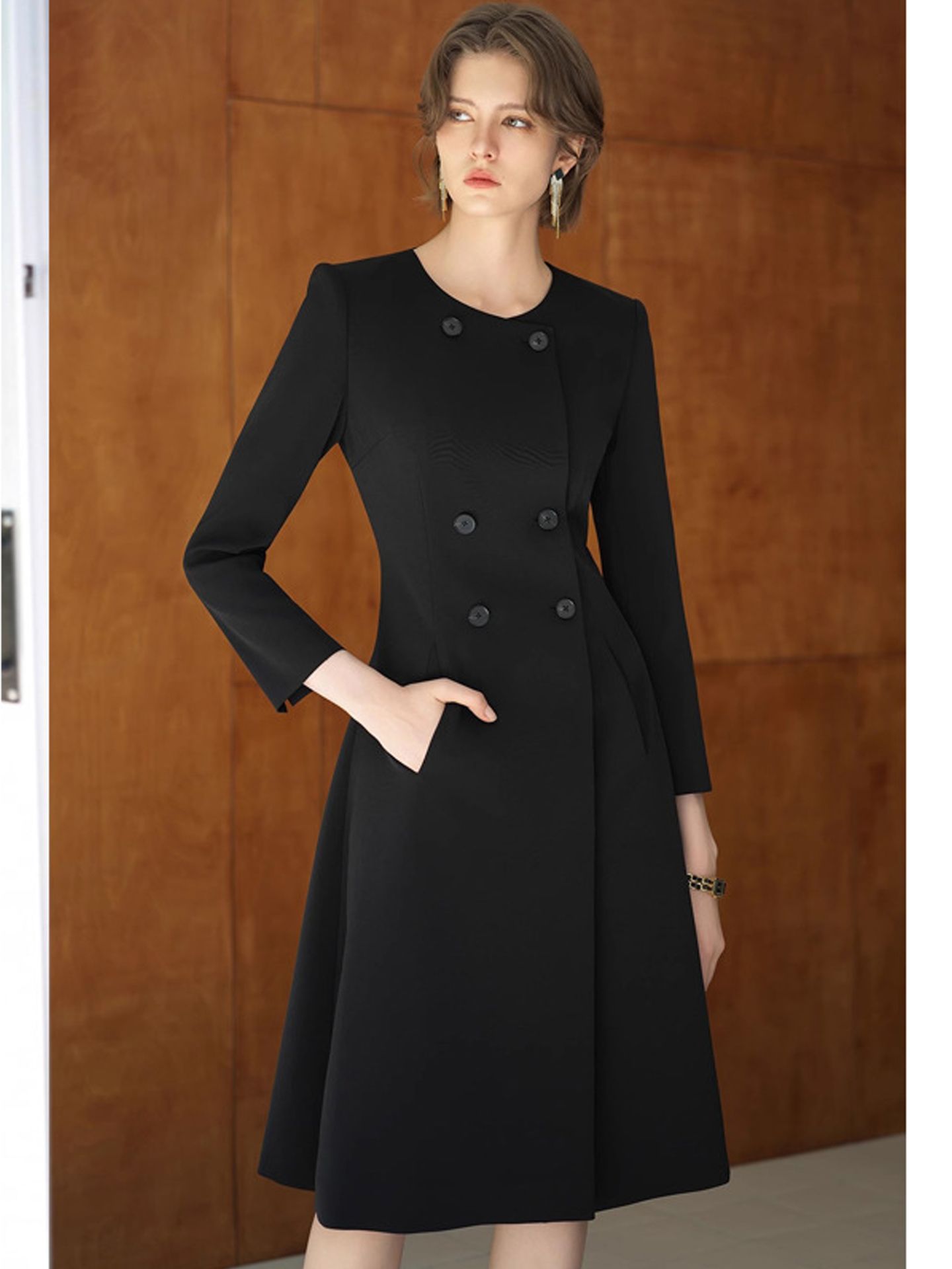 A stylish, elegant dress in trench coat style with a fitted waistline, a round neckline, and a long, flowing skirt in black.