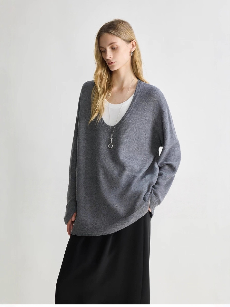 A minimalist sweater with a deep V-neck and ruffled edges, paired with a skirt for a layered look.