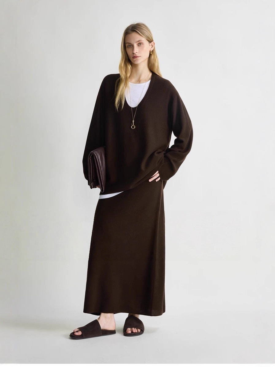 A minimalist sweater with a deep V-neck and ruffled edges, paired with a skirt for a layered look.