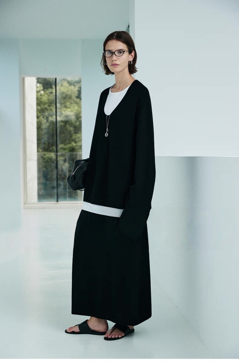 A minimalist sweater with a deep V-neck and ruffled edges, paired with a skirt for a layered look.